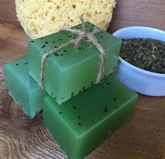 Luxury handmade green glycerin soap bars with natural ingredients and essential oils, placed next to a rustic sponge and a bowl of dried herbs.